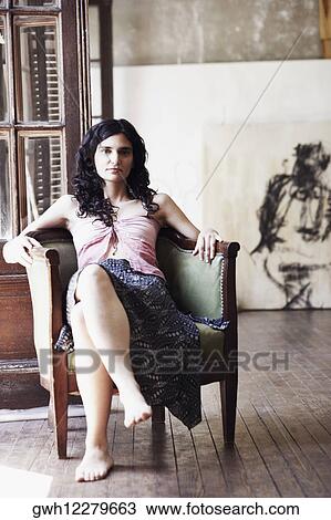 Stock Image - Portrait of a mid adult woman sitting in an armchair with her legs crossed. Fotosearch