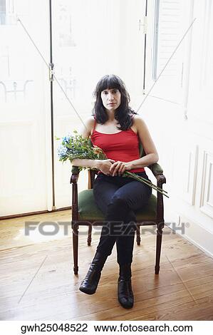 Stock Image - Portrait of a mid adult woman sitting in an armchair and holding a bunch of flowers. Fotosearch