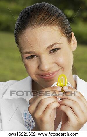 Stock Image - Portrait of a teenage girl tearing open a condom packet and smiling. Fotosearch