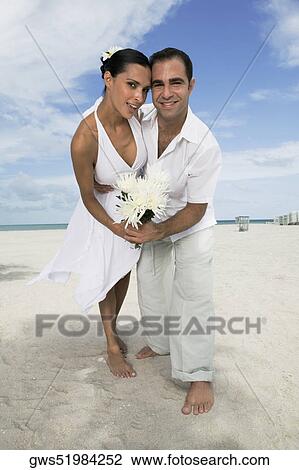 Stock Image - Portrait of a young couple dancing on the beach and holding flowers. Fotosearch