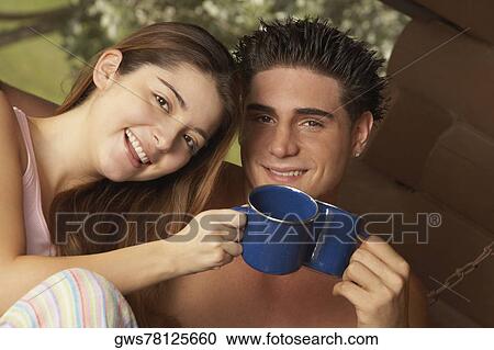 Stock Image - Portrait of a young couple toasting cups of tea and smiling. Fotosearch