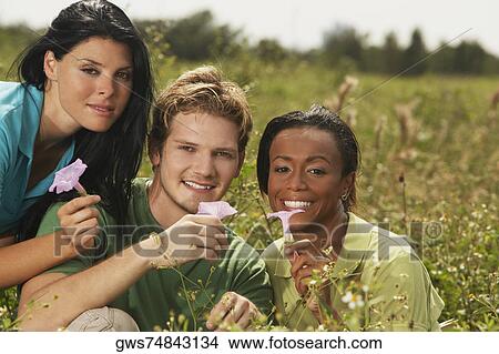 Picture - Portrait of a young man and two young women holding flowers. Fotosearch