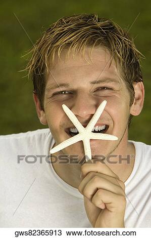 Portrait of a young man holding a starfish in front of his mouth View Large Photo Image Stock Image - Portrait of a young man holding a starfish in front of his mouth. Fotosearch
