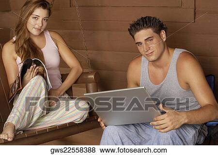 Portrait of a young man holding a laptop with a young woman sitting on a porch swing View Large Photo Image Stock Photo - Portrait of a young man holding a laptop with a young woman sitting on a porch swing. Fotosearch