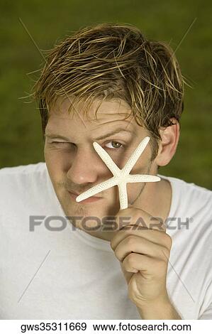 Portrait of a young man holding a starfish in front of his eye View Large Photo Image Stock Photo - Portrait of a young man holding a starfish in front of his eye. Fotosearch