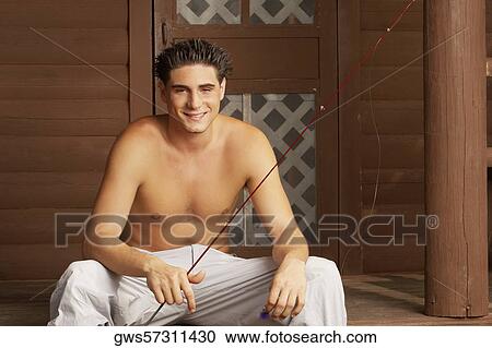 Stock Image - Portrait of a young man sitting on a ledge and holding a fishing rod. Fotosearch