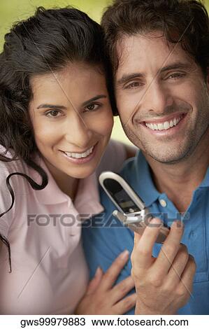 Stock Image - Portrait of a young woman and a mid adult man holding a mobile phone. Fotosearch