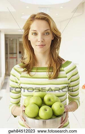 Stock Image - Portrait of a young woman holding a bowl of green apples. Fotosearch