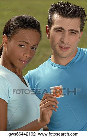 Portrait of a young woman holding a condom with a mid adult man standing beside her View Large Photo Image Stock Image - Portrait of a young woman holding a condom with a mid adult man standing beside her. Fotosearch