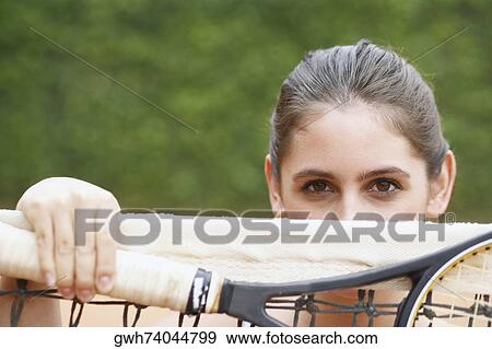 Stock Photo - Portrait of a young woman holding a tennis racket over a tennis net. Fotosearch