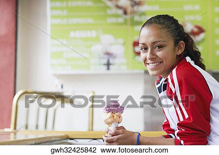 Stock Image - Portrait of a young woman holding an ice-cream and smiling. Fotosearch