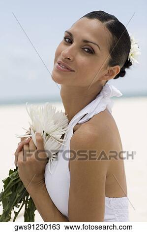 Stock Image - Portrait of a young woman holding flowers on the beach. Fotosearch