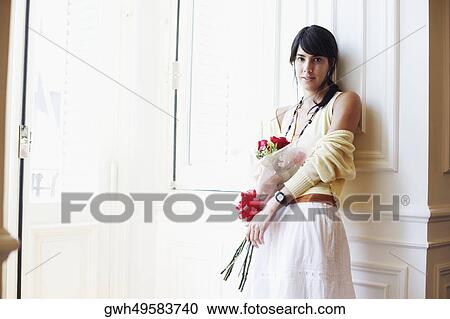 Portrait of a young woman leaning against a wall and holding a bouquet of flowers View Large Photo Image Stock Image - Portrait of a young woman leaning against a wall and holding a bouquet of flowers. Fotosearch