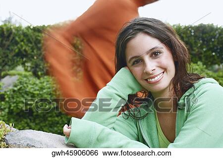 Stock Photograph - Portrait of a young woman leaning against a stone and smiling. Fotosearch