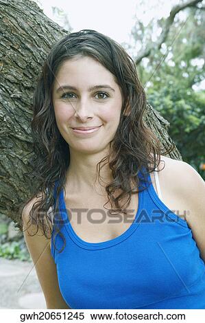 Portrait of a young woman leaning against a tree trunk and smiling View Large Photo Image Stock Photography - Portrait of a young woman leaning against a tree trunk and smiling. Fotosearch