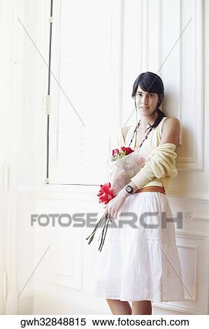 Stock Photography - Portrait of a young woman leaning against a wall and holding a bouquet of flowers. Fotosearch