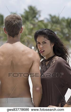 Stock Photograph - Portrait of a young woman making a face and standing beside a young man. Fotosearch