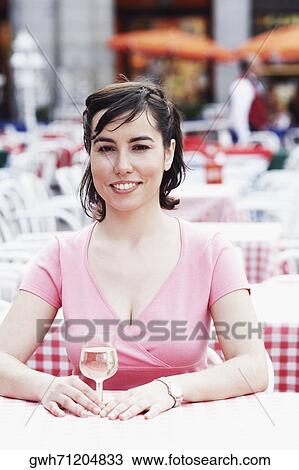 Stock Image - Portrait of a young woman sitting at a table in a sidewalk cafe . Fotosearch