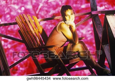 Picture - Portrait of a young woman sitting in an Adirondack chair and smiling. Fotosearch