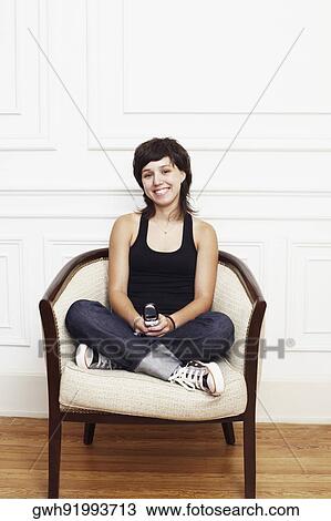 Stock Image - Portrait of a young woman sitting in an armchair and holding a mobile phone. Fotosearch