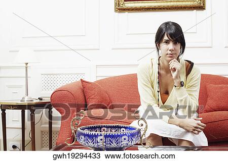 Portrait of a young woman sitting on a couch with her hand on her chin View Large Photo Image Stock Image - Portrait of a young woman sitting on a couch with her hand on her chin. Fotosearch