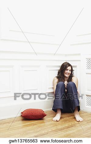 Stock Image - Portrait of a young woman sitting on the floor at the corner of a room. Fotosearch