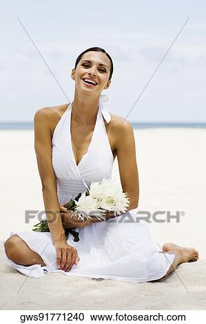 Stock Image - Portrait of a young woman sitting on the beach and smiling. Fotosearch