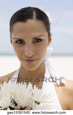 Stock Image - Portrait of a young woman smiling and holding flowers on the beach. Fotosearch
