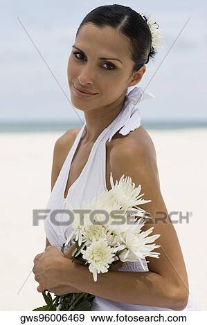 Portrait of a young woman smiling and holding flowers on the beach View Large Photo Image Stock Photo - Portrait of a young woman smiling and holding flowers on the beach. Fotosearch