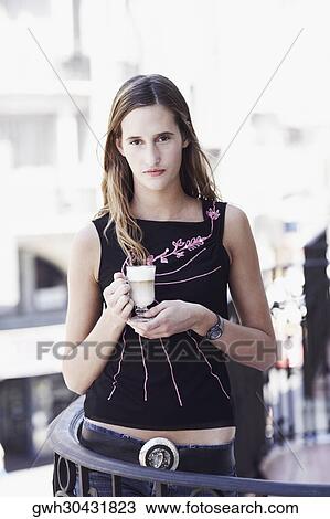 Portrait of a young woman standing in the balcony and holding a glass of coffee View Large Photo Image Stock Image - Portrait of a young woman standing in the balcony and holding a glass of coffee . Fotosearch