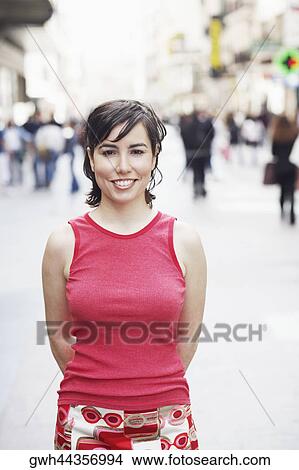 Portrait of a young woman standing with her hands behind her back View Large Photo Image Picture - Portrait of a young woman standing with her hands behind her back . Fotosearch