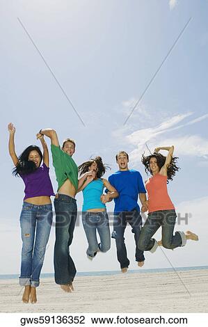 Stock Image - Portrait of five young people jumping on the beach. Fotosearch