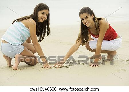 Stock Photograph - Portrait of two girls drawing in sand on the beach. Fotosearch