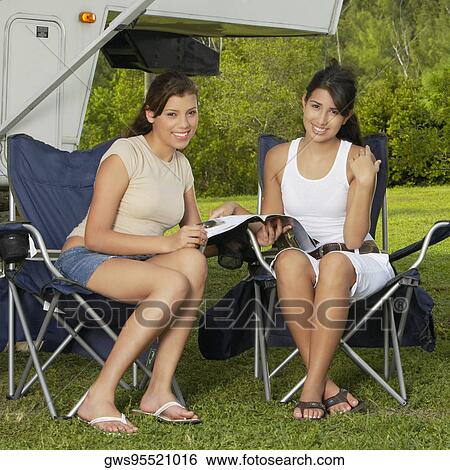 Stock Photograph - Portrait of two young women sitting on folding chairs and smiling. Fotosearch