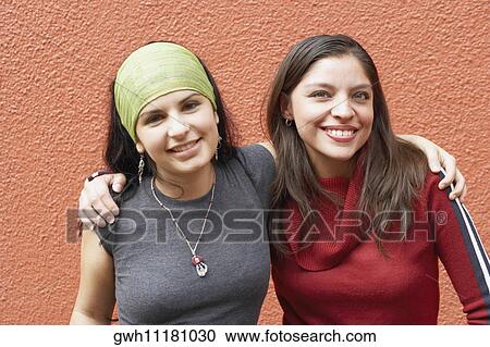 Stock Image - Portrait of two young women with their arms around each other. Fotosearch
