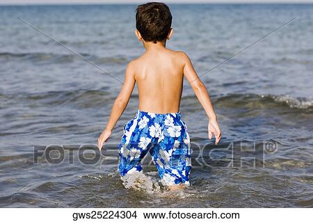 Picture - Rear view of a boy walking in water. Fotosearch