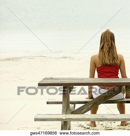 Rear view of a girl sitting on a bench at the beach View Large Photo Image Stock Photograph - Rear view of a girl sitting on a bench at the beach. Fotosearch