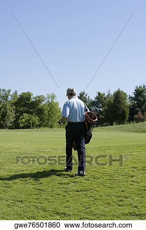 Stock Image - Rear view of a man carrying a golf bag. Fotosearch
