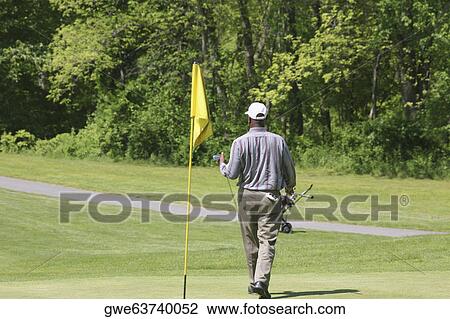 Stock Image - Rear view of a man carrying a golf club on a golf course. Fotosearch