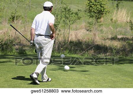 Stock Image - Rear view of a man holding a golf club and walking on a golf course. Fotosearch