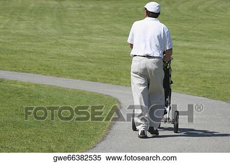 Rear view of a man pushing a golf trolley View Large Photo Image Stock Photography - Rear view of a man pushing a golf trolley. Fotosearch