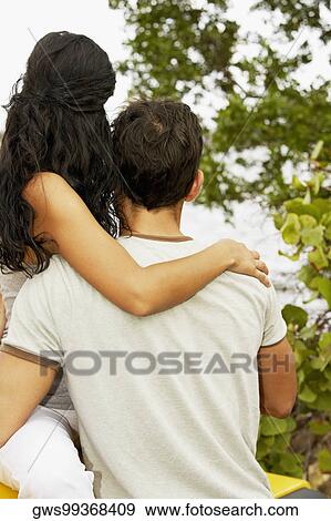 Stock Photo - Rear view of a mid adult man and a young woman with their arms around each other. Fotosearch