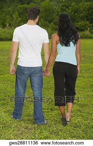 Rear view of a mid adult man and a young woman holding hands and walking View Large Photo Image Stock Photograph - Rear view of a mid adult man and a young woman holding hands and walking. Fotosearch