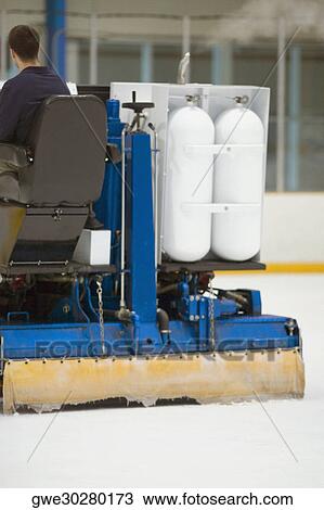 Stock Image - Rear view of a person sitting on an ice resurfacing machine. Fotosearch