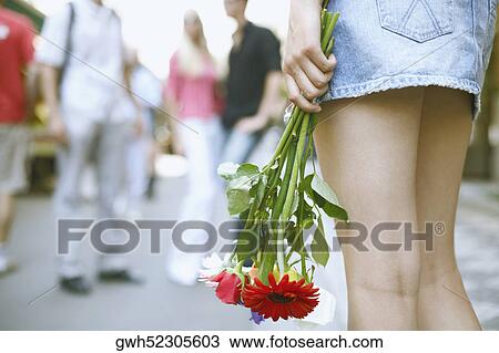 Stock Image - Rear view of a woman holding a bouquet of flowers . Fotosearch