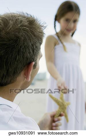 Stock Image - Rear view of a young man giving a starfish to a girl. Fotosearch
