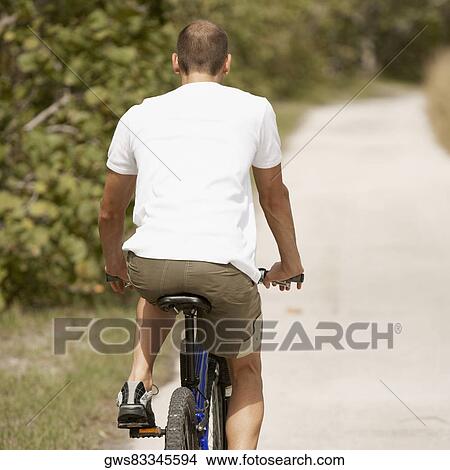 Picture - Rear view of a young man riding a bicycle. Fotosearch