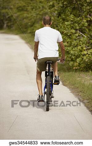Rear view of a young man riding a bicycle View Large Photo Image Stock Image - Rear view of a young man riding a bicycle. Fotosearch