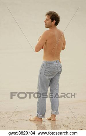 Rear view of a young man standing on the beach and looking sideways View Large Photo Image Picture - Rear view of a young man standing on the beach and looking sideways. Fotosearch