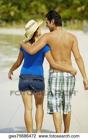 Rear view of a young man walking on the beach with his arm around a teenage girl View Large Photo Image Stock Image - Rear view of a young man walking on the beach with his arm around a teenage girl. Fotosearch